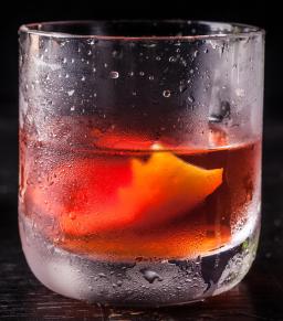 Sazerac-cocktail viskilasissa jääkuution ja sitruunankuorikiehkuran kanssa