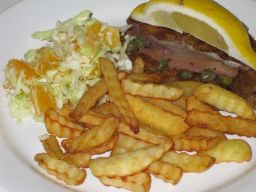 Wieninleike ranskalaisten perunoiden sekä kaali-appelsiinisalaatin kera lautasella